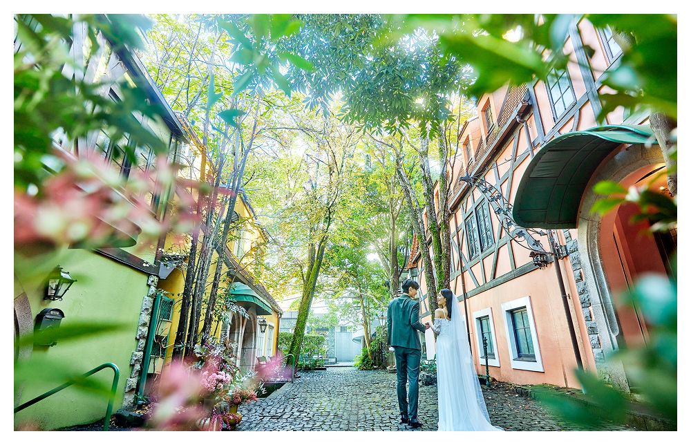 メゾン・シンフォニークの敷地内の緑豊かな石畳の小道に立つ新郎新婦